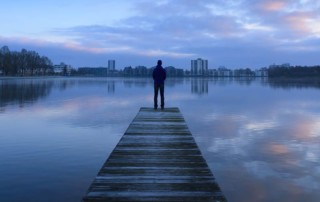 Mann am Bootssteg blickt auf Wasser und Skyline