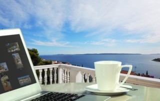 Laptop und Kaffeetasse auf einem Tisch mit Blick aufs Meer